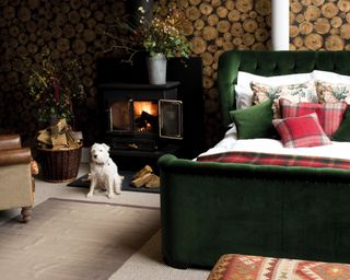 Green velvet bed frame with green, red and white assortment of cushions with traditional black fireplace and white dog sat on floor