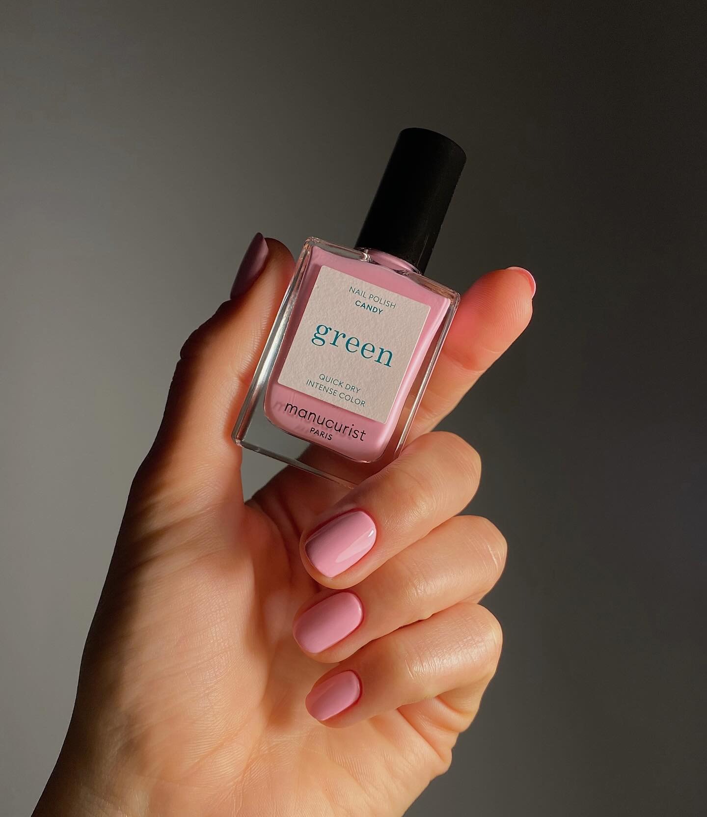 A hand holding a Manucurist green flash polish bottle with pink nails