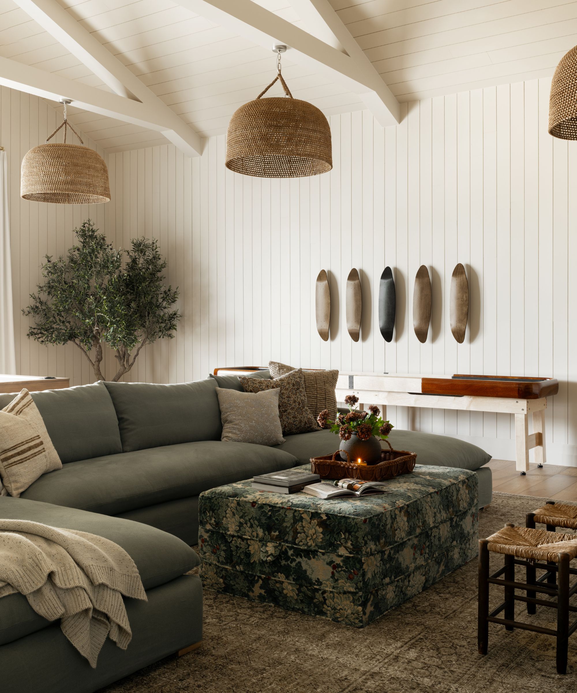 a tongue and groove paneled family room by Shea McGee with large rattan pendant lights, a green sectional, tapestry print ottoman and east coast style decor