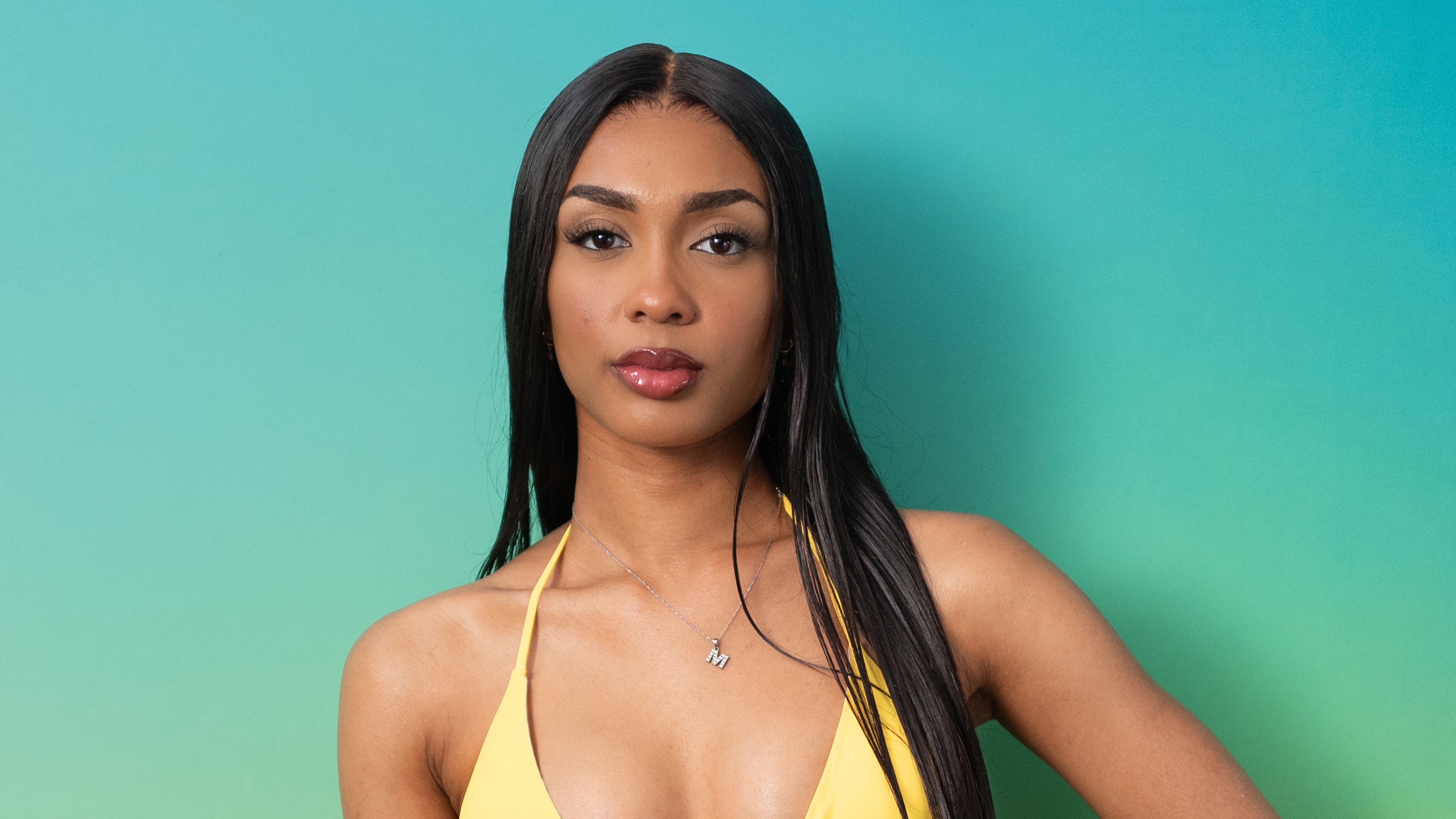 Bombshell Malisha standing against a green background in swimwear and smiling.