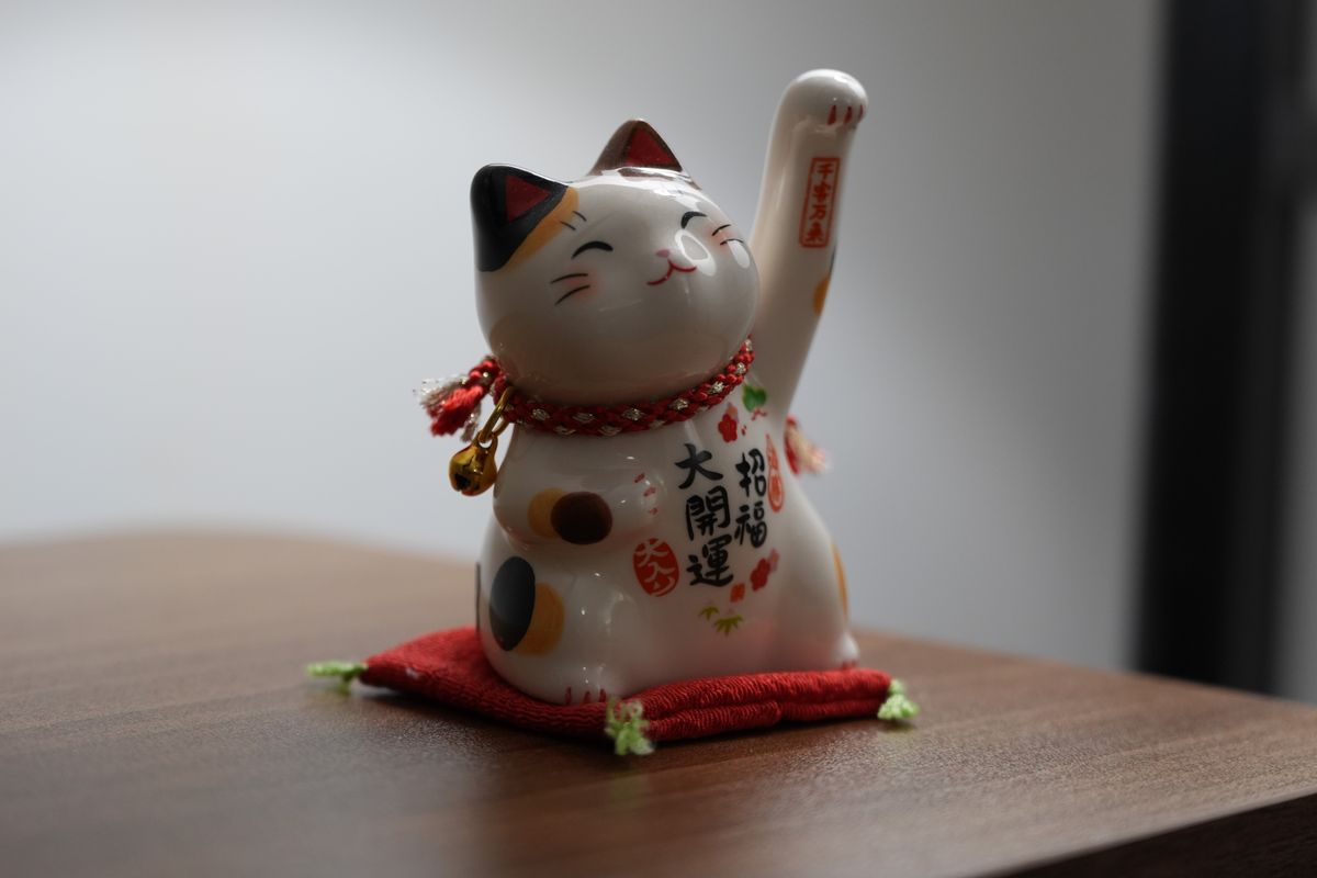 Ceramic lucky cat ornament sitting on a red cushion indoors.