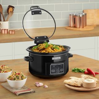 Crockpot black slow cooker on wooden kitchen bench with curry and rice being served