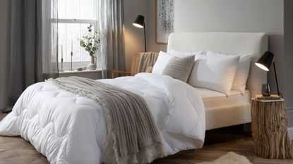 A bed with a white comforter and throw blanket