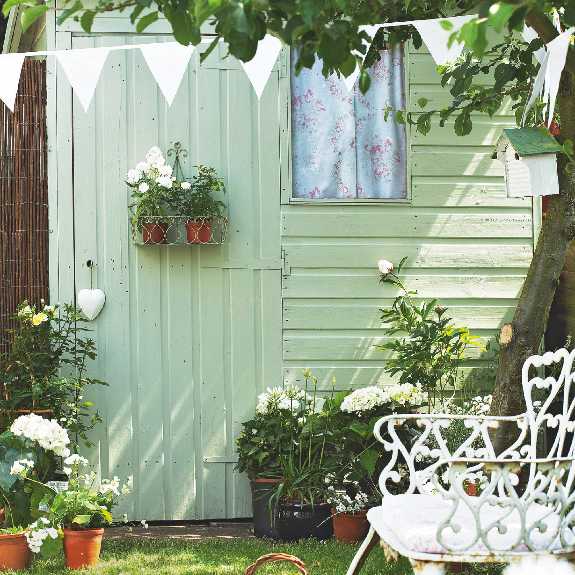 Sage green shed with white bunting, bench and accessories.
