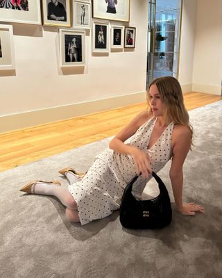 Woman wears a white polka dot Realisation Par halter dress with white tights and beige kitten heels.