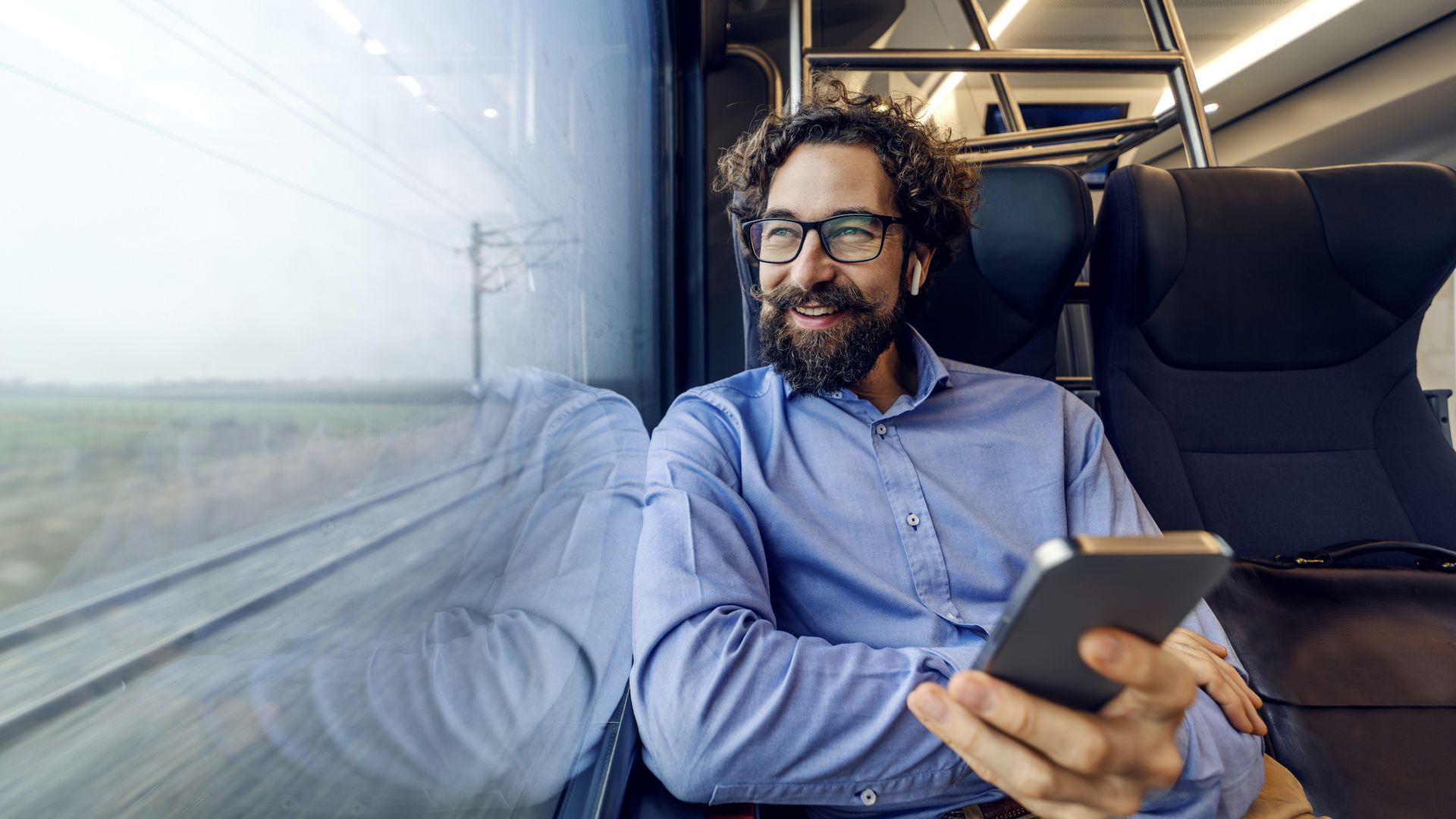 A man looking out of the train window, while listening to music.