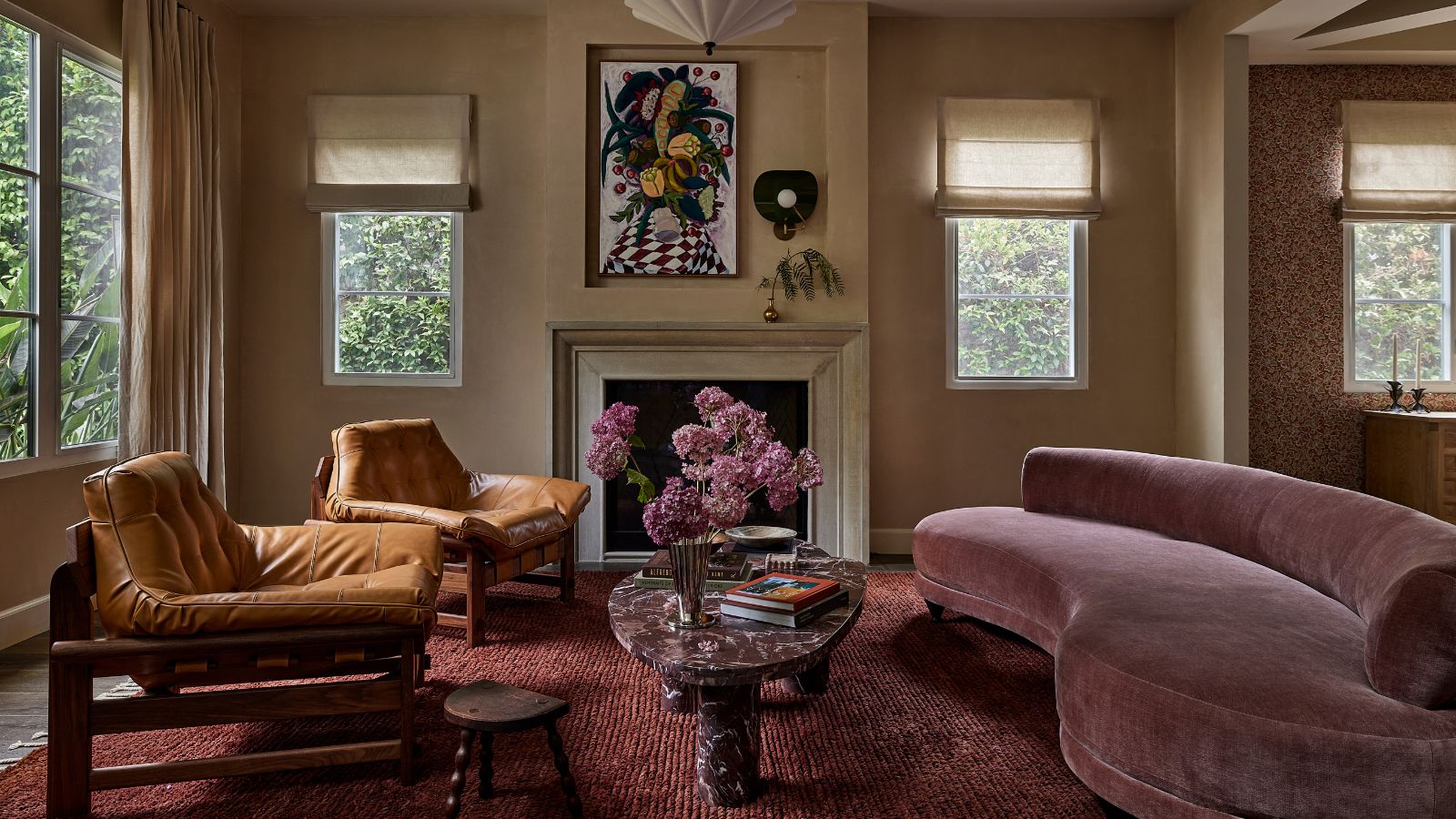 A modern living room with neutral walls, a fireplace, a plum-colored rug and a mauve curved sofa. 