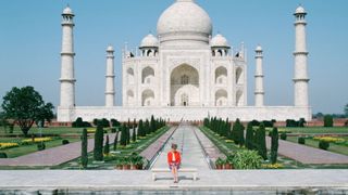 Princess Diana sat on a bench in front of the Taj Mahal in India, there are no other tourists and she is in a red blazer sat alone