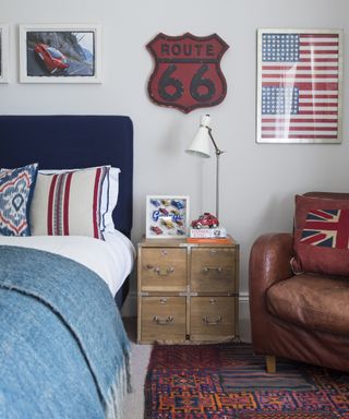 A teenage boys bedroom idea with blue headboard, Americana artwork, white walls and brown leather armchair