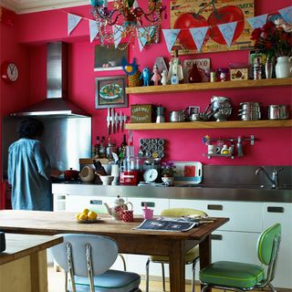 kitchen with pink wall wooden shelf white cabinets and wooden dinning table and chairs