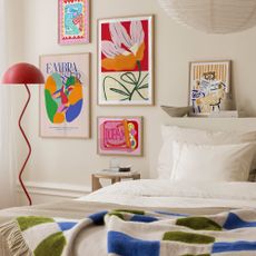 A bedroom with colourful prints on the wall and a red floor lamp