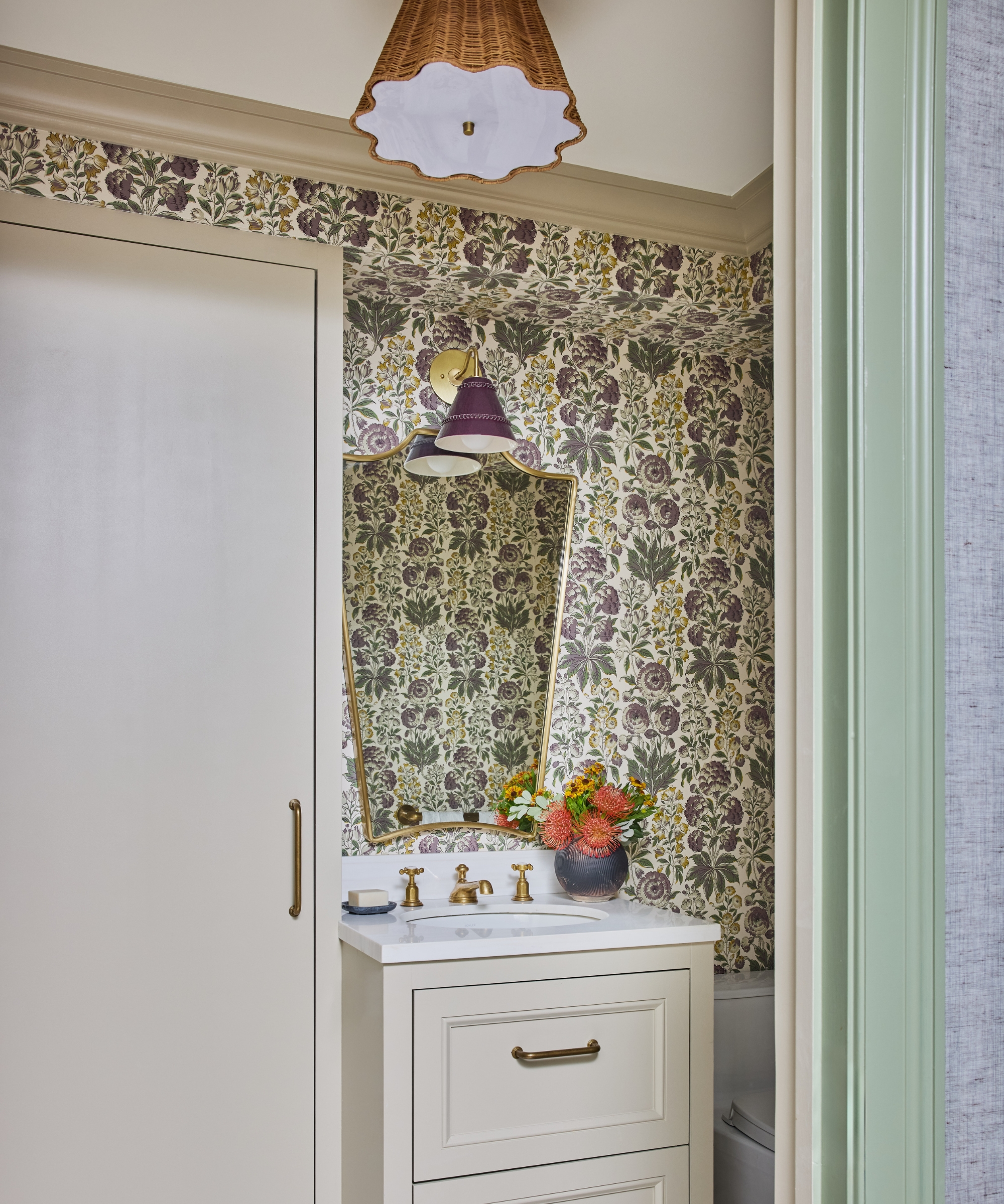 Powder room with floral wallpaper, cream vanity, brass taps, hexagon marble floor tiles and an asymmetric mirror.