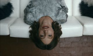 a woman (Sofia Vergara as Griselda Blanco) leans over the back of a white sofa
