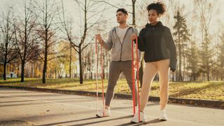 Man and woman performing one arm biceps curl with resistance bands in a park