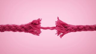 pink frayed rope hanging on by one thread against pink background