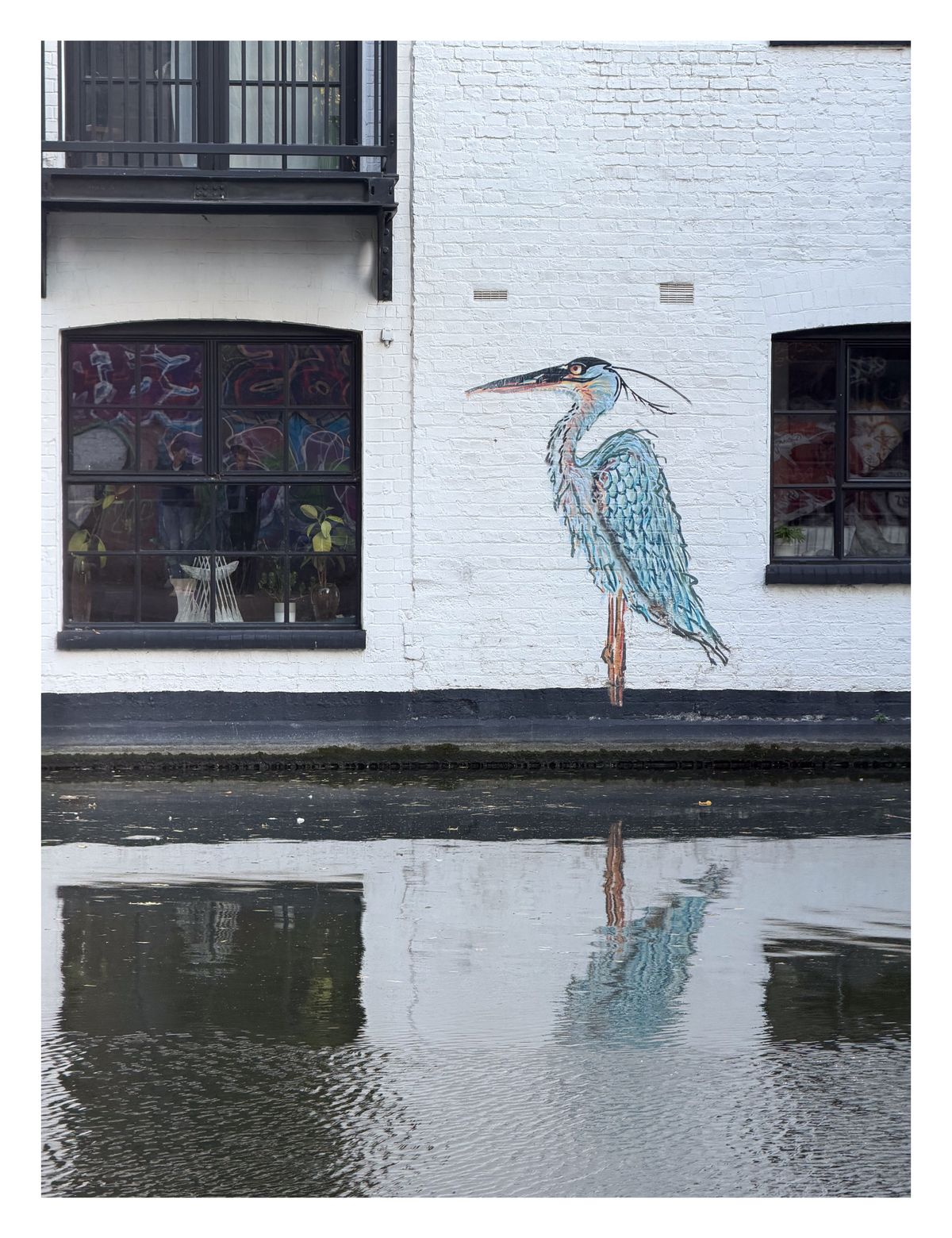 A painting of a heron on a white wall next to a canal