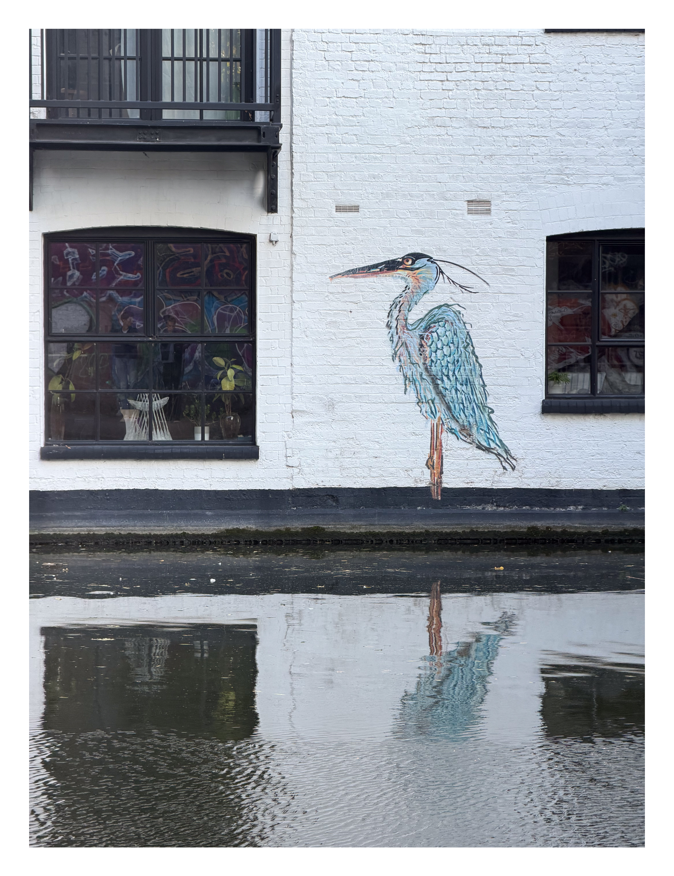 A painting of a heron on a white wall next to a canal