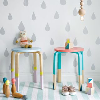 Light wood stools with colourful painted legs in front of a wallpapered wall