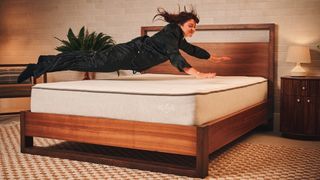 A member of our mattress testing team jumps onto the Nolah Original All Foam Mattress on a bed frame in a bedroom. She dives onto the bed ready to hit the cushioned comfort layers