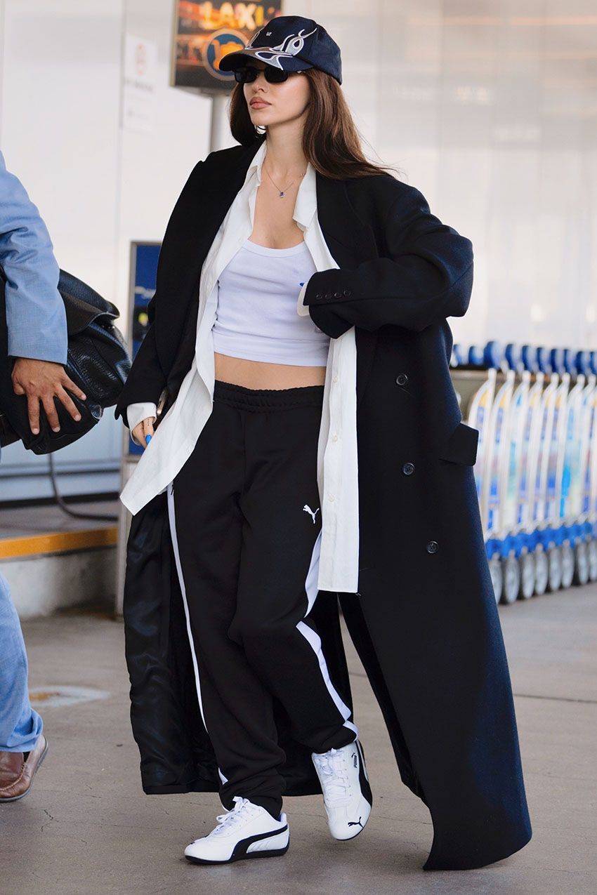 Dove Cameron wearing a black coat, white tank top, black track pants, and puma sneakers