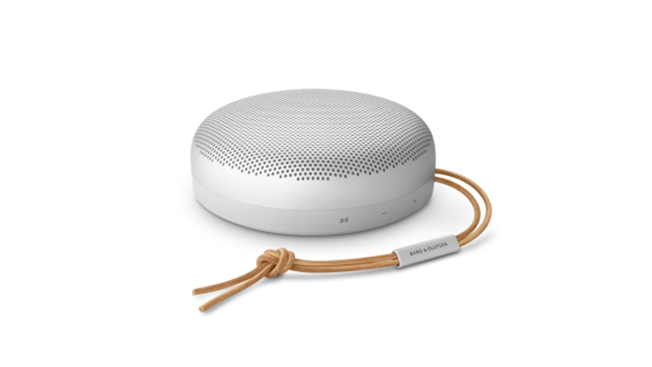 The beosound a1 bluetooth speaker in silver, with a brown carrying strap