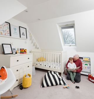A children's bedroom with a white colour scheme including a cost, chest of drawers and bookshelves for children's picture books