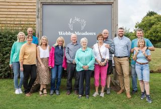 A mixed group of middle aged and senior people standing together under a sign that says Webb's Meadow