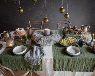 Scandinavian Christmas decor table ideas, green baubles, green table runners, cream table cloth, candle wreath, fruit, cake, white bowls, grey plates