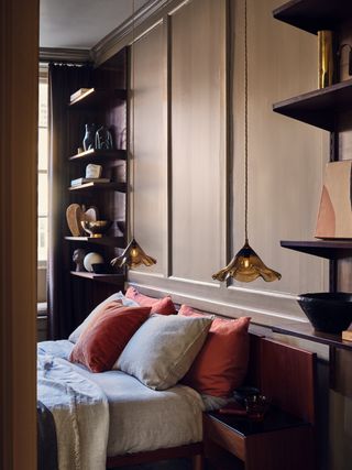 taupe bedroom with wooden open shelving, two amber glass pendant lights, rust and oatmeal cushions