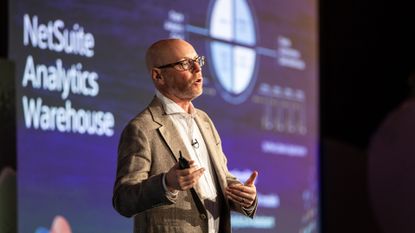 A telephoto shot of Evan Goldberg, founder and EVP at Oracle NetSuite, pictured from the waist up speaking onstage at the opening keynote of SuiteConnect London 2025.