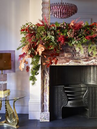 floral garland on ornate marble mantel, glass and gold side table with lamp