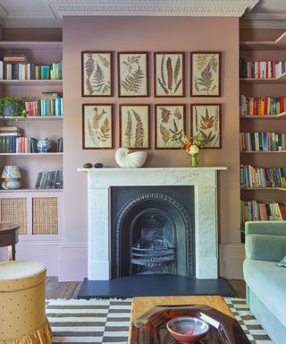 A pink living room with tall built-in bookshelves, a white fireplace, and a collage of framed artwork
