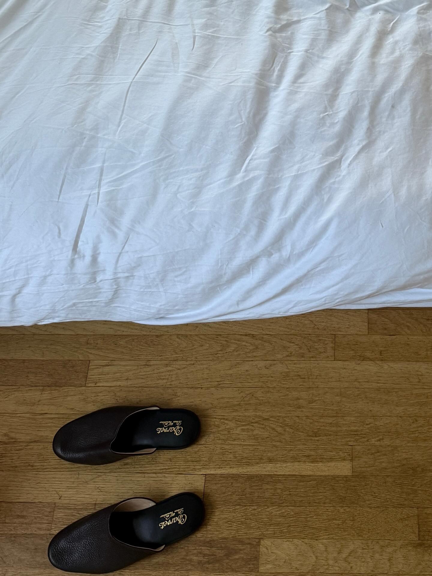 A white bed with Charvet slippers on the floor.