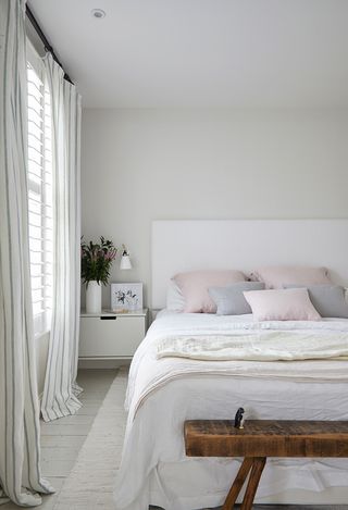 White bedroom with pastel bedding and rustic wooden bench
