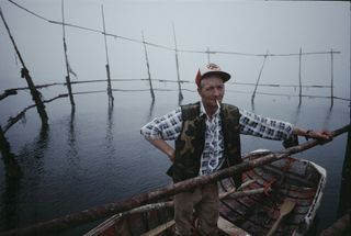 a fisherman in a small boat on the water with cigarette in mouth