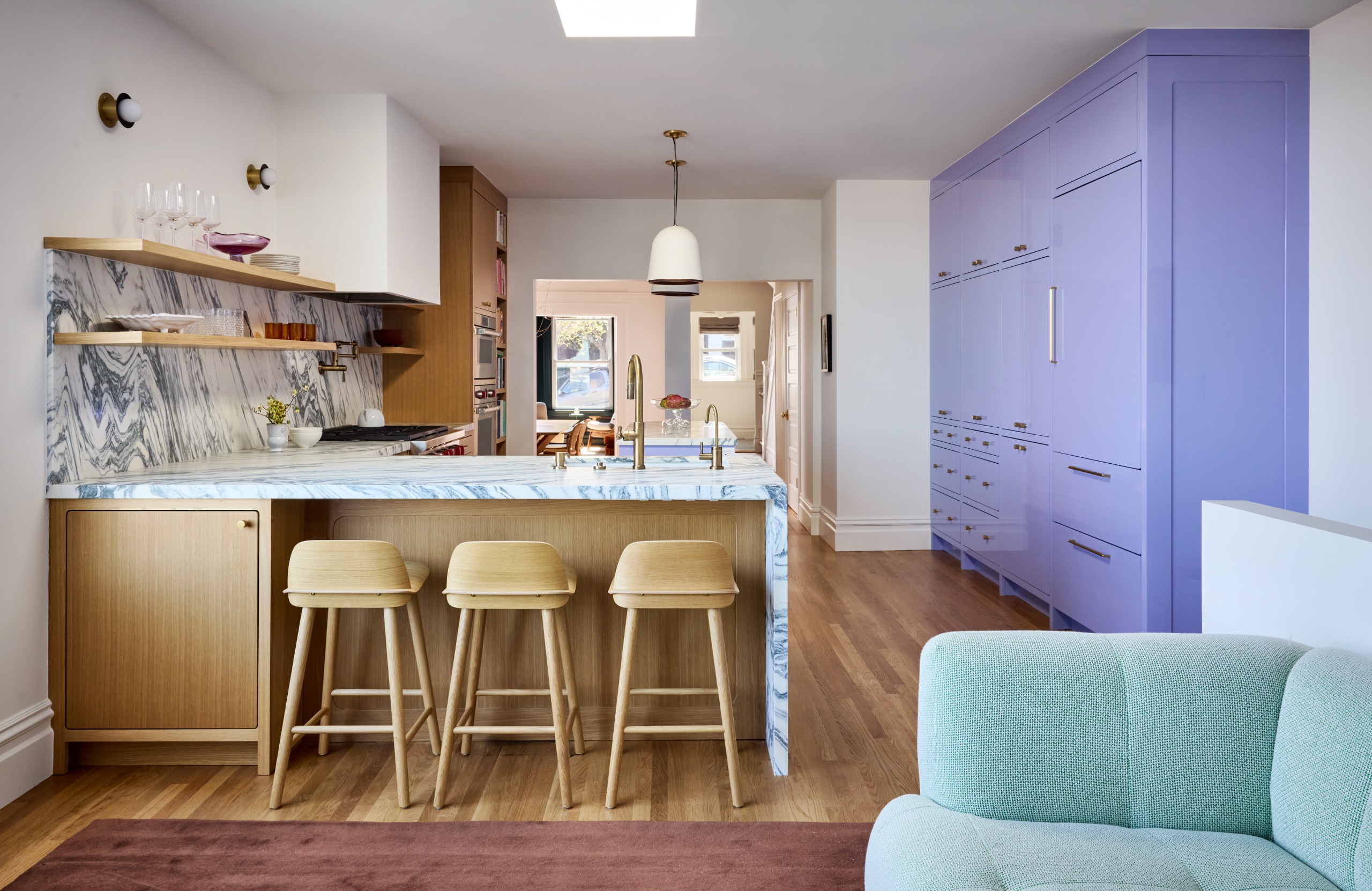 A modern marble and wood kitchen with a bold pop of periwinkle cabinetry running along one side