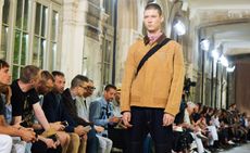 male model on a fashion week runway wearing a camel coloured jacket and cross body bag