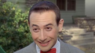 Paul Reubens grinning outside as Pee Wee Herman in Pee Wee's Big Adventure.