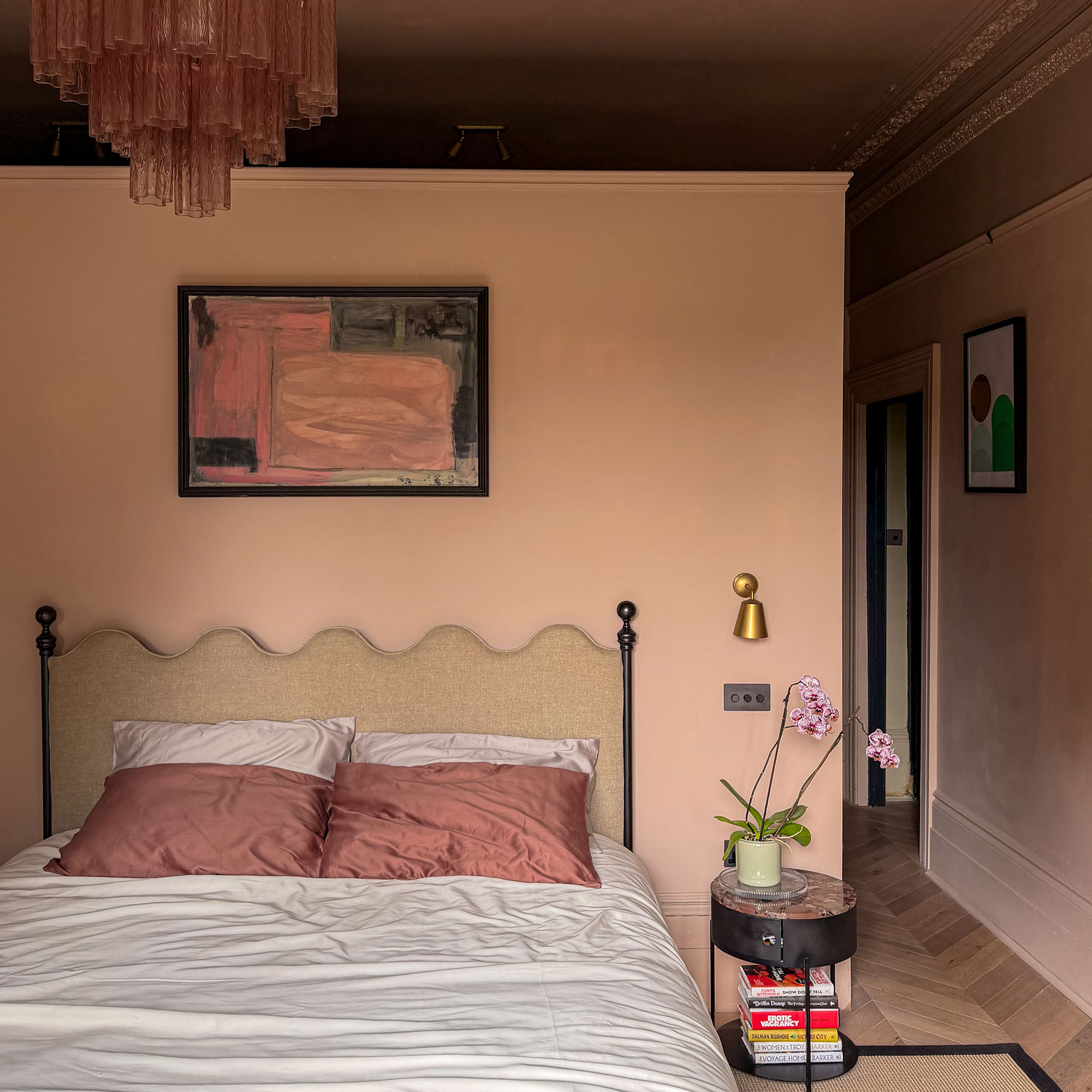 Peach bedroom with wavy headboard, abstract art above bed, and small round bedside table with orchid