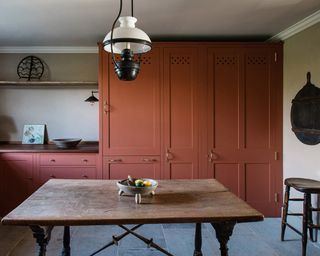 Terracotta red kitchen with raw wooden dining area and brass handles on cabinetry