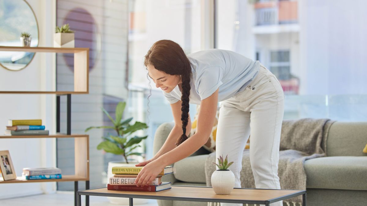 Woman picking up pile of books on table