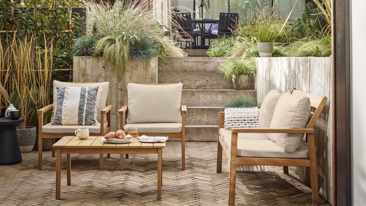 paved patio with sofas, planters filled with ornamental grasses and steps leading up to the house