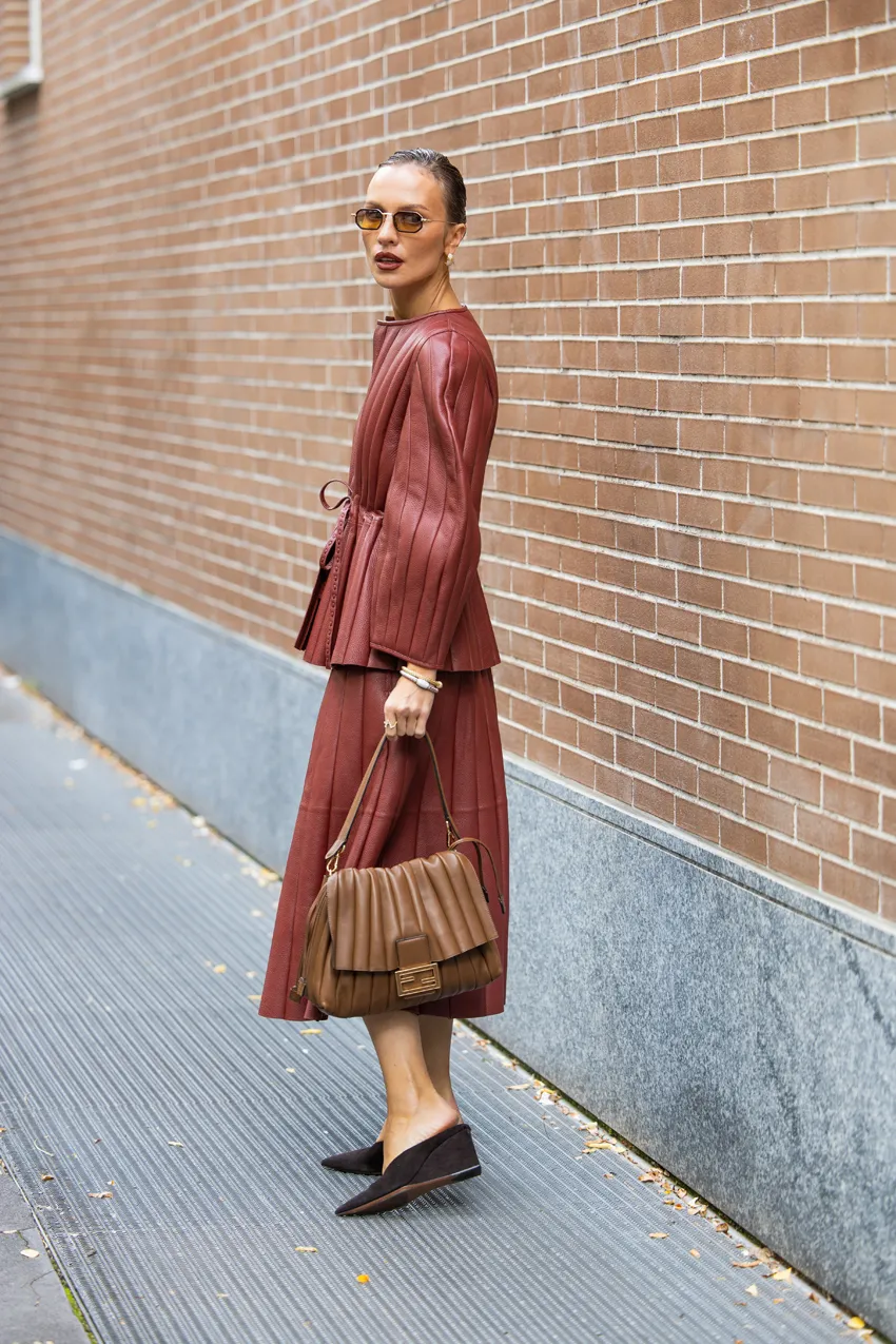 A woman wears closed-toe wedge mules with a leather top and leather skirt and fendi bag.