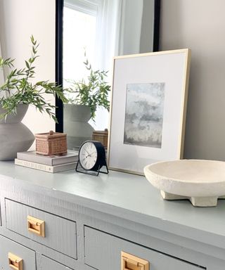 A blue dresser with a mirror, photo frame, and plant on it