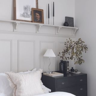 Bedroom with cream wall panelling behind bed and longline shelf.