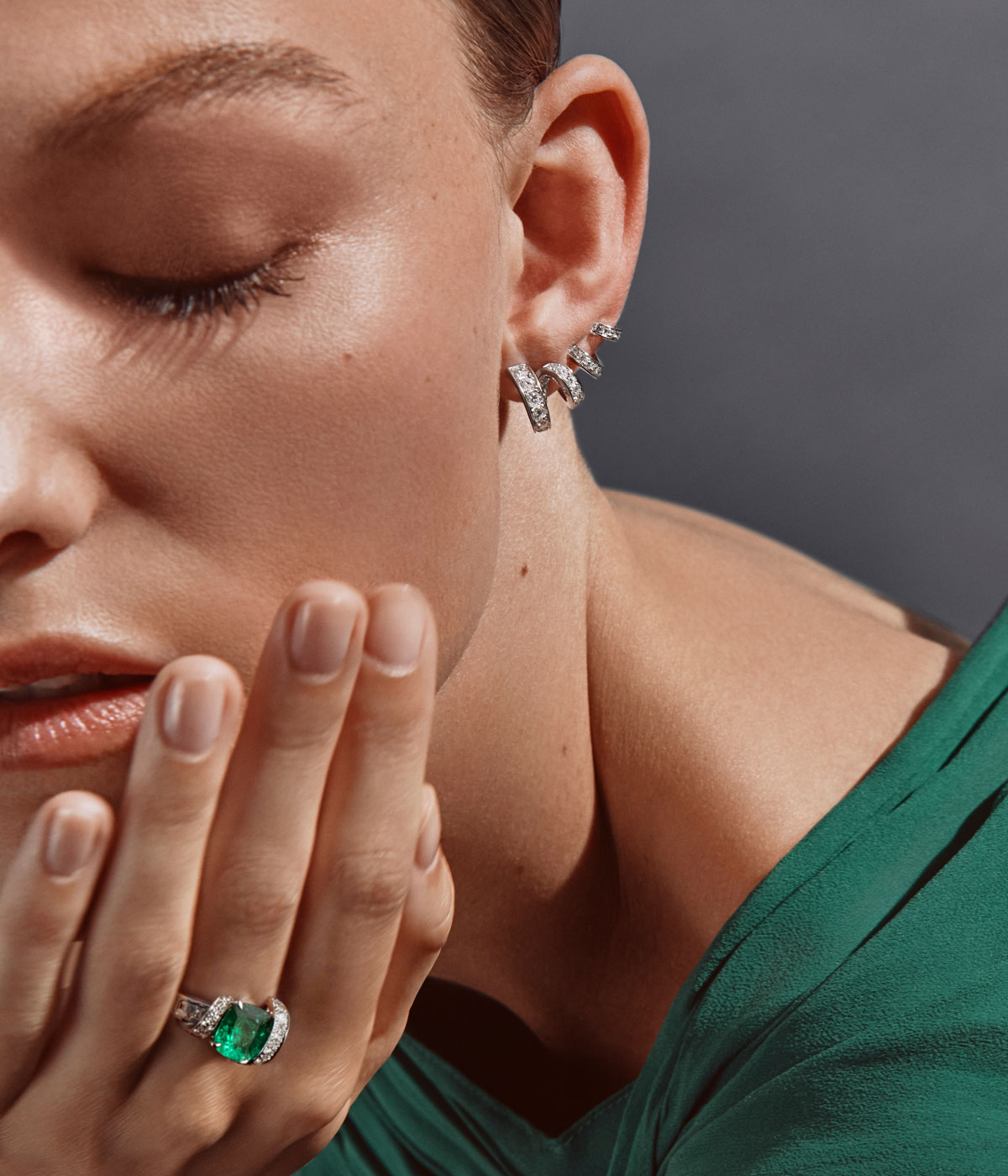 Woman wearing a twirl diamond earring and diamond and emerald ring