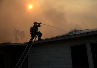 Taken on January 9, 2025 in Altadena, California, a firefighter is seen on the roof of a burning home affected by the Eaton Fire