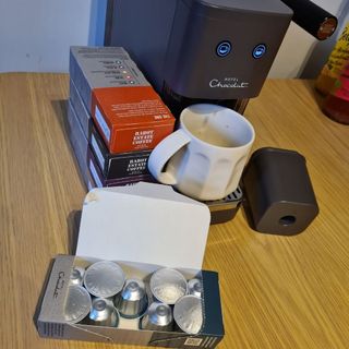 Hotel Chocolat Podster next to stacked boxes of coffee pods
