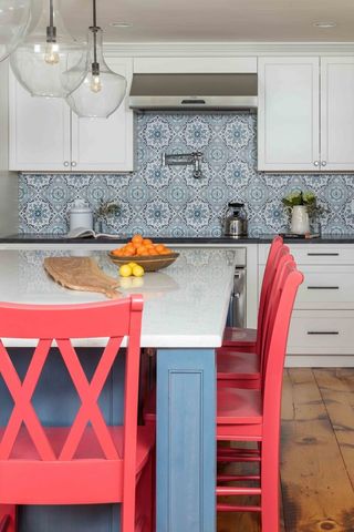 Red kitchen chairs against a blue breakfast bar with white countertop, patterned backsplash and white glossy units.