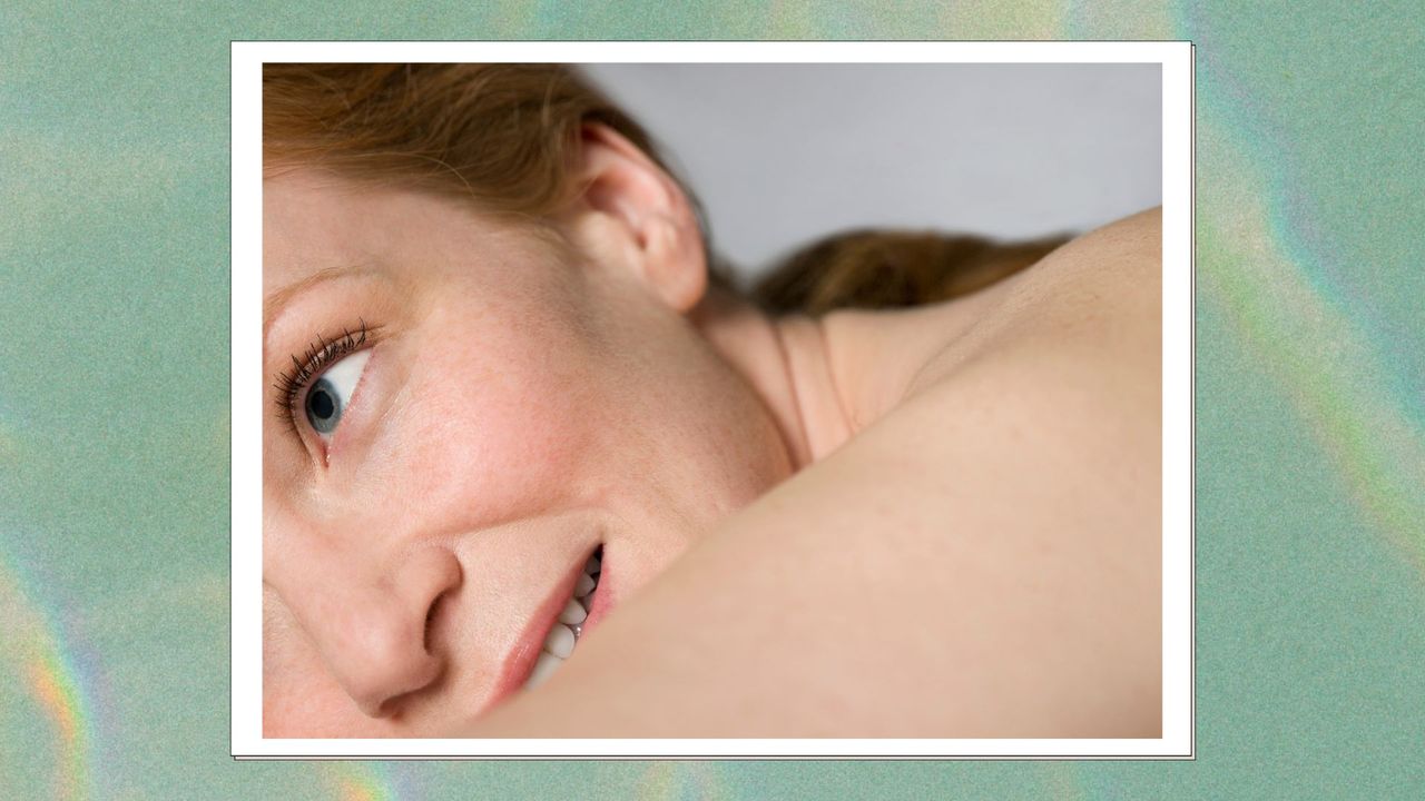 a woman with red hair and beautiful skin pictured close up, lying down on a green backdrop